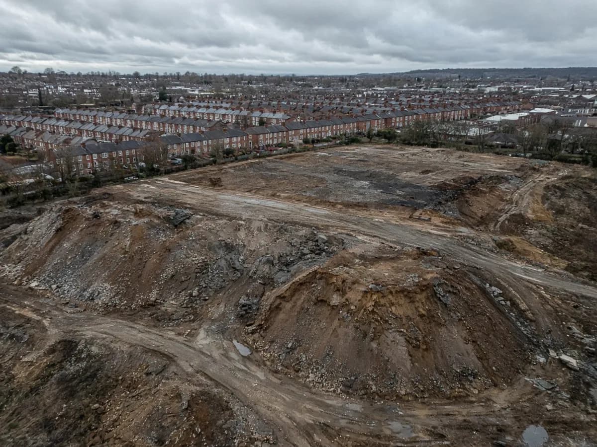 Aerial-looking view of a UK brownfield plot with earth mounds and distant terraces